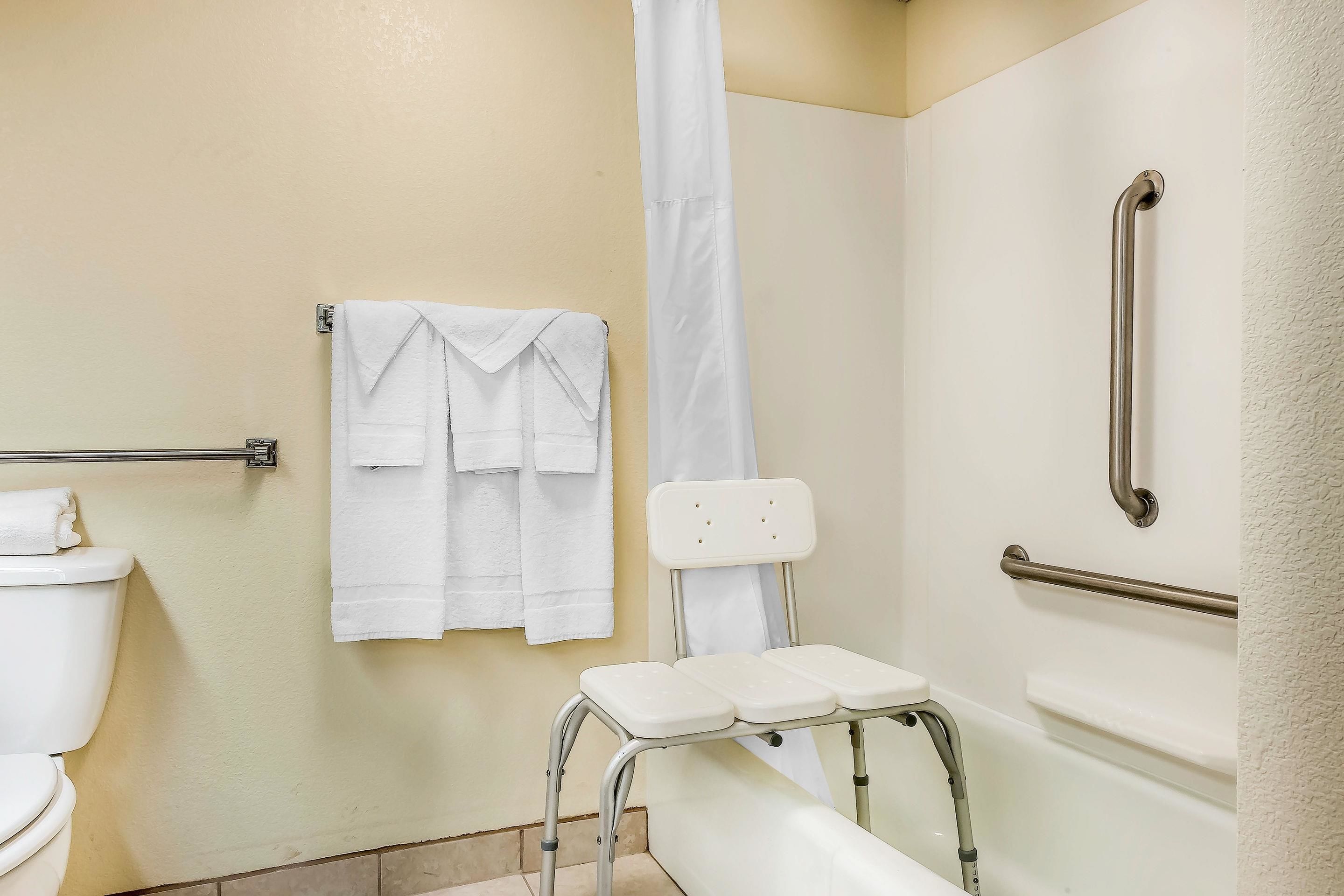 Une salle de bain comprenant des toilettes, une douche avec un rideau blanc, une baignoire blanche et une barre d’appui.