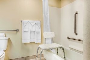A bathroom with a toilet, a shower with a white curtain, a white bathtub, and a grab bar.