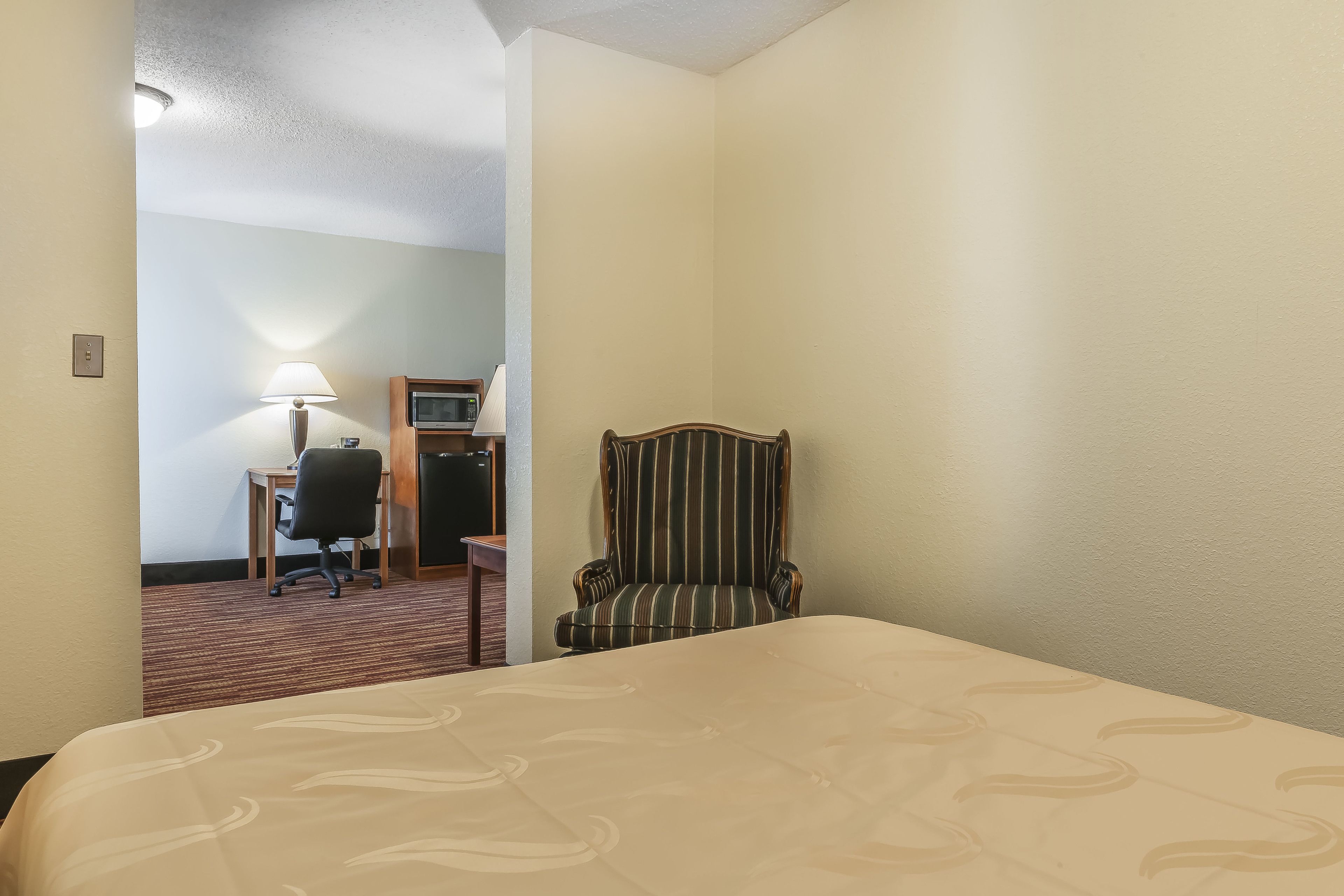 Ein Hotelzimmer mit einem Bett, einem Schreibtisch mit Lampe, einem Fernseher und einem gestreiften Sessel.