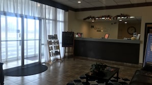 Zona de recepción de un hotel, con mostrador, un reloj y vistas al exterior.