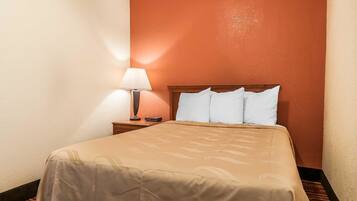 Una habitación de hotel con cama, mesita de noche, lámpara y una pared pintada de naranja cálido.