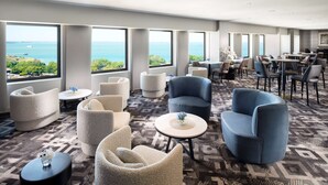 Un hall d’hôtel spacieux, doté de plusieurs espaces salon, de grandes fenêtres offrant une vue sur l’océan et d’un tapis à motifs.