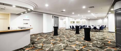 A spacious hotel lobby with a reception desk, multiple tables, and chairs arranged for dining or meetings.