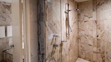 Un baño moderno con paredes de mármol, cabina de ducha de vidrio y un perchero visible.