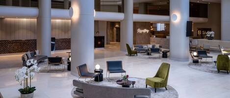 A spacious lobby with high ceilings, large columns, and a variety of seating arrangements including sofas, chairs, and a round table.