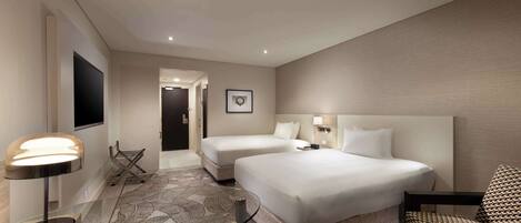 A hotel room with two beds, a glass table, a lamp, a patterned rug, and a chair.