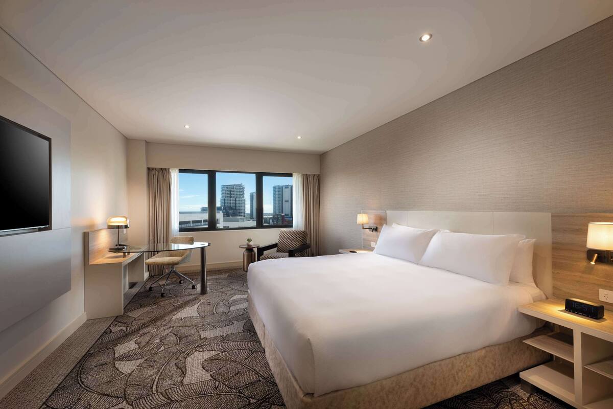 A hotel room with a large bed, a desk with a chair, a TV, and a window with curtains.
