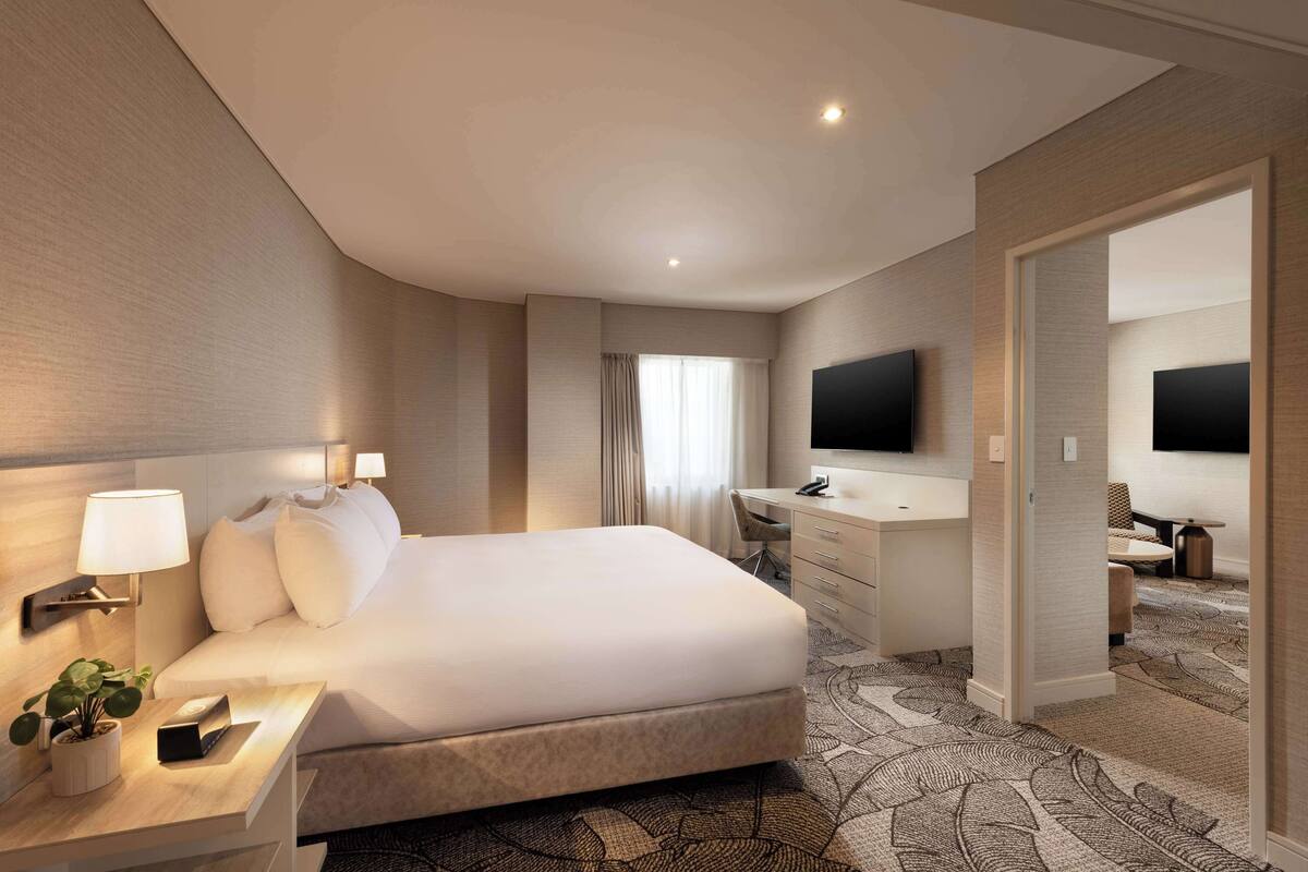 A modern hotel room with a large bed, a desk with a chair, a flat-screen TV, and a walk-in closet.