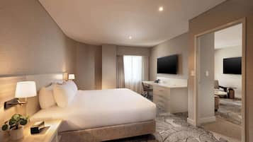 A modern hotel room with a large bed, a desk with a chair, a flat-screen TV, and a walk-in closet.