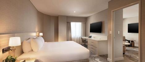 A modern hotel room with a large bed, a desk with a chair, a flat-screen TV, and a walk-in closet.