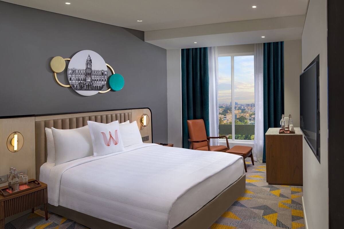 Une chambre d’hôtel avec un grand lit, un bureau, une chaise, une télévision et une vue sur la ville.