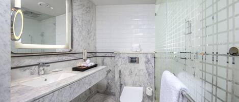 A modern bathroom with a marble sink, a large mirror, a toilet, and a glass shower enclosure.