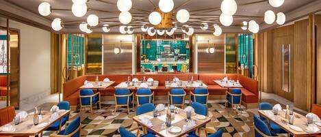 Un restaurante con mesas redondas, sillas azules y una zona de bar central.