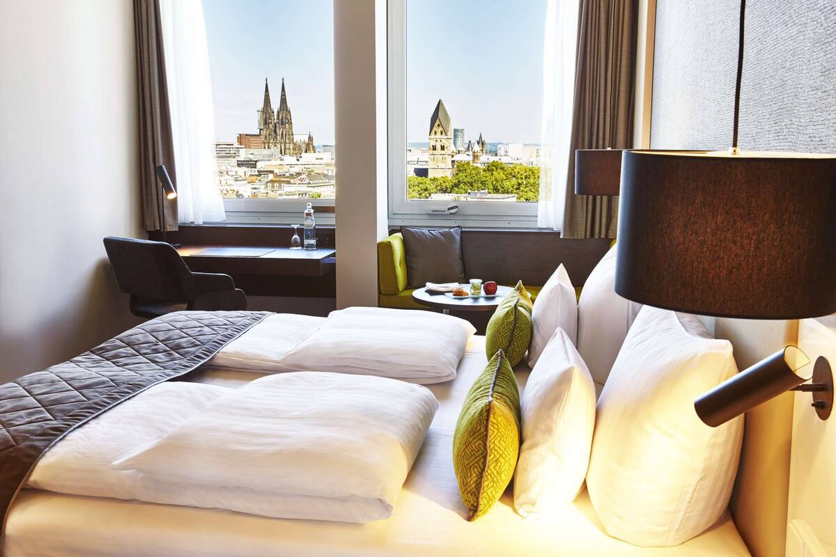 Habitación de hotel con cama, escritorio y vista a un paisaje urbano.