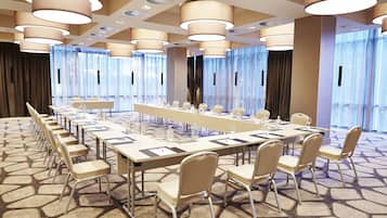Une salle de conférence avec une longue table, des chaises et de grandes fenêtres équipées de rideaux.