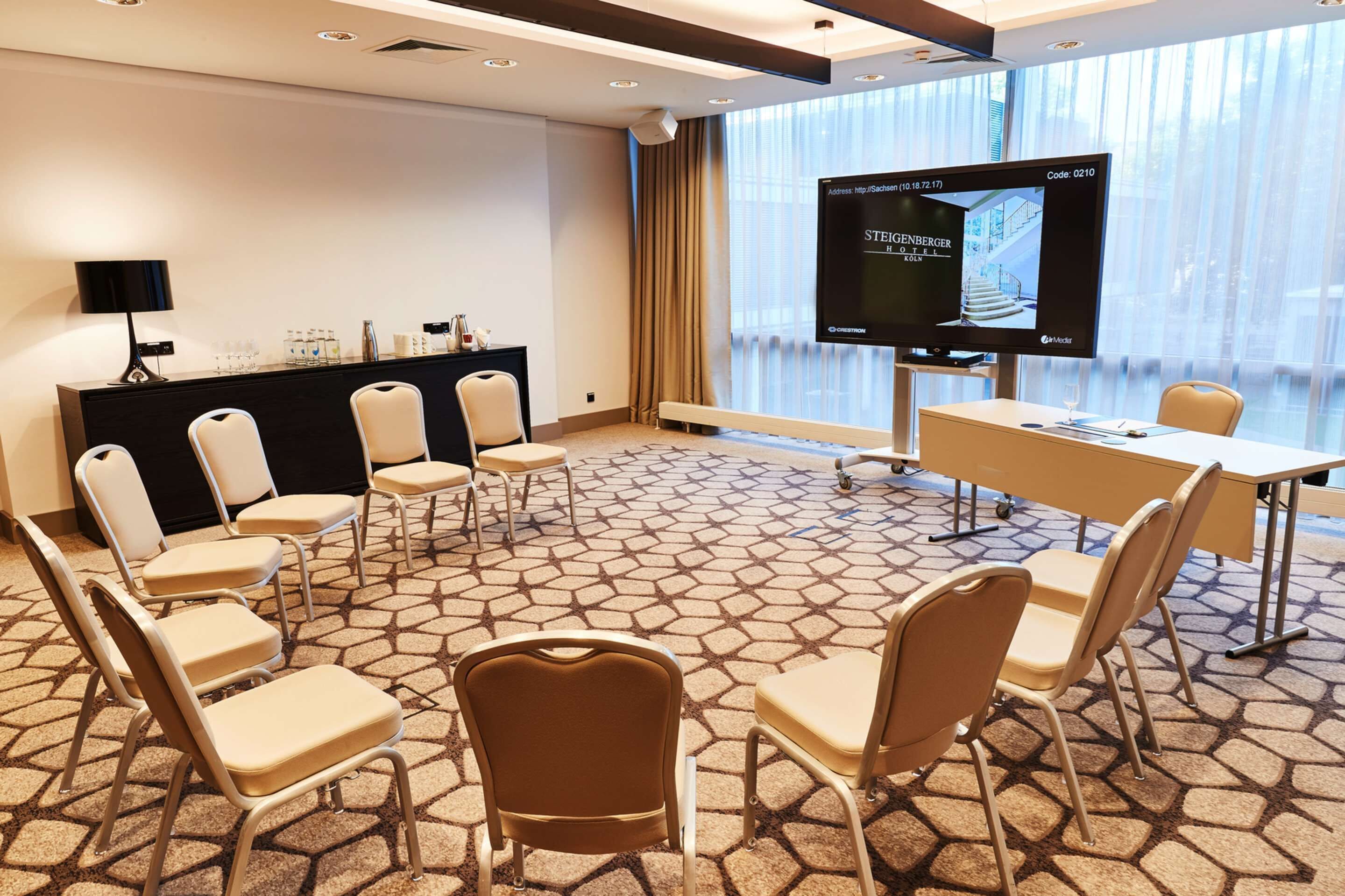 Une salle de conférence équipée d’un grand écran, d’un pupitre et de plusieurs chaises disposées autour d’une table.