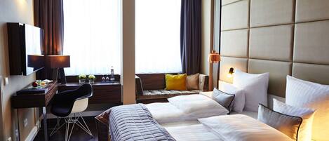 Habitación de hotel con dos camas, un escritorio, una silla y un amplio ventanal con cortinas.