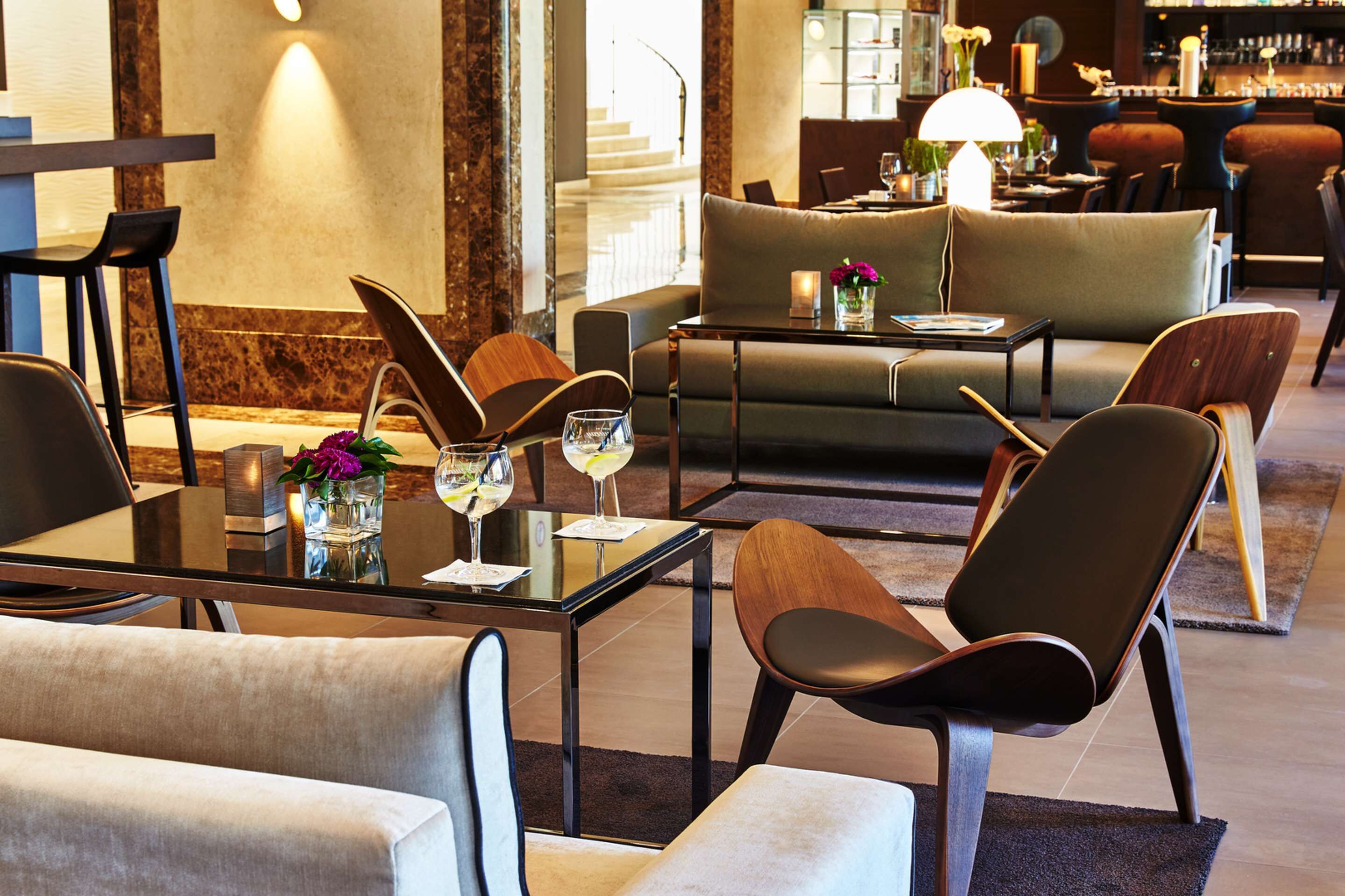 A modern hotel lobby with a glass table, leather chairs, a sofa, and a bar area.