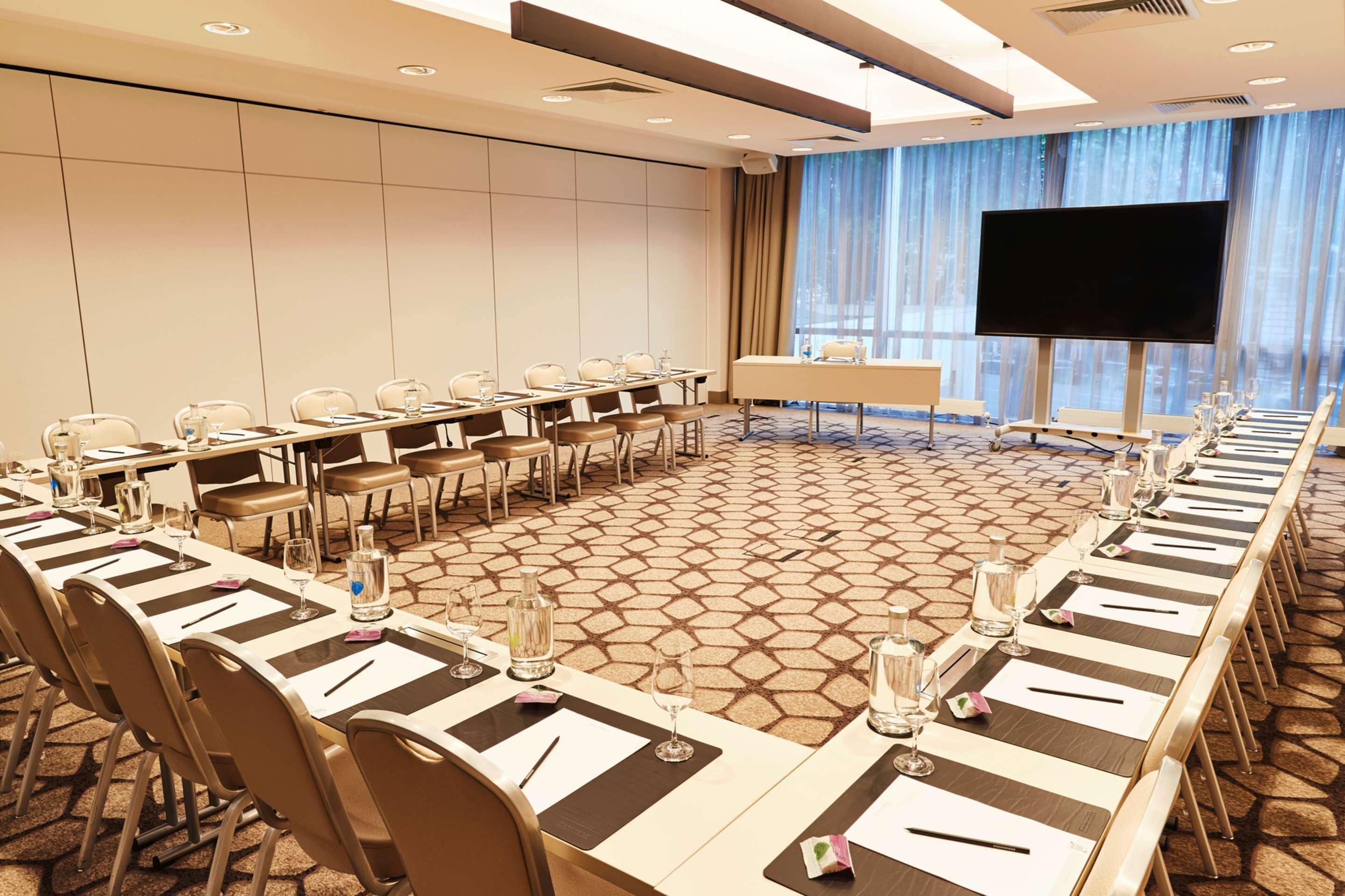 Un salón de conferencias con una larga mesa dispuesta para reuniones, una pantalla grande y vistas al exterior a través de amplios ventanales.
