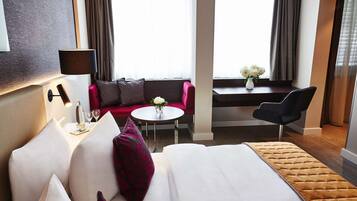 Une chambre d’hôtel avec un lit, un canapé, une petite table sur laquelle est posé un vase de fleurs, une lampe et une chaise.