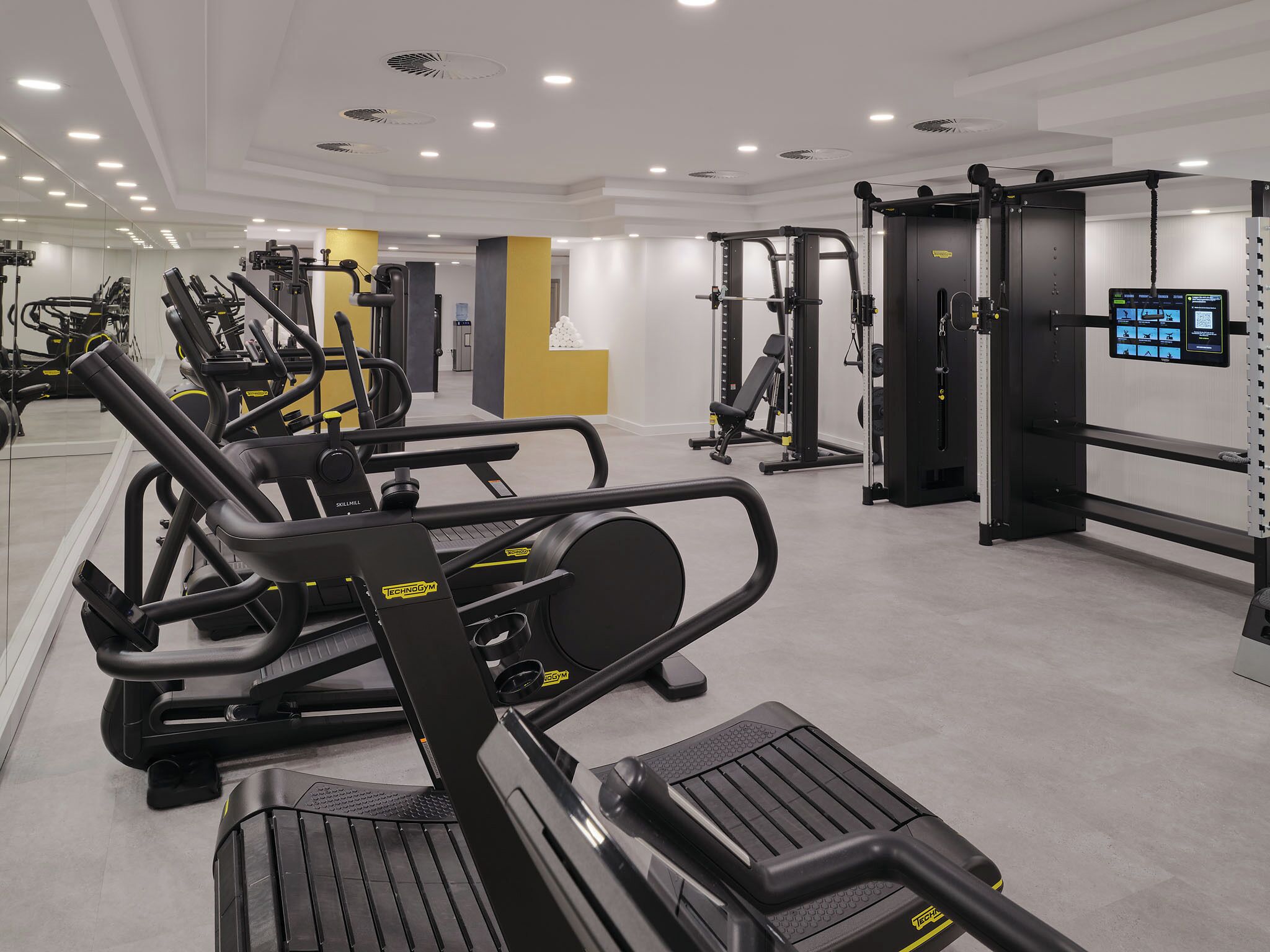 A modern gym with cardio machines, weightlifting equipment, and a digital display.