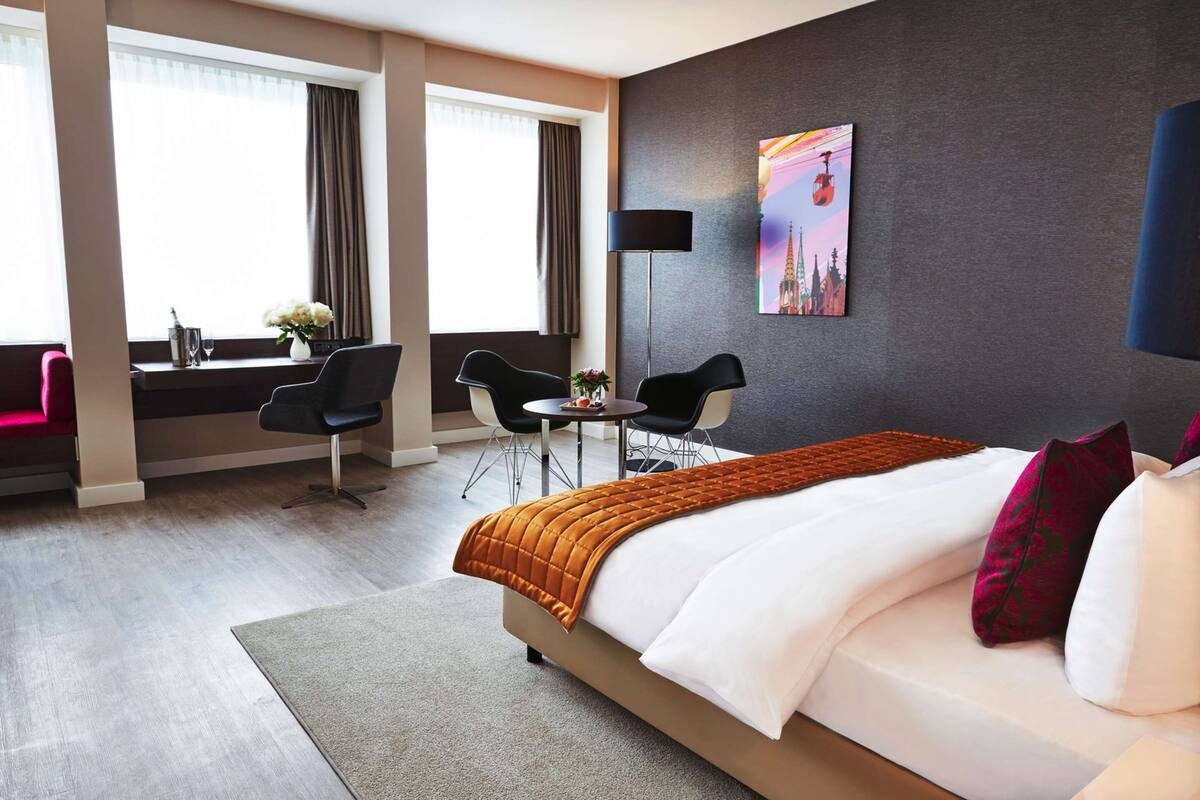 Una habitación de hotel con una cama grande, un escritorio con dos sillas, una mesita y un cuadro en la pared.