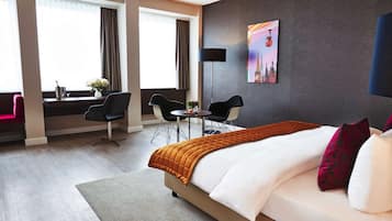 Ein Hotelzimmer mit einem großen Bett, einem Schreibtisch mit zwei Stühlen, einem kleinen Tisch und einem Bild an der Wand.