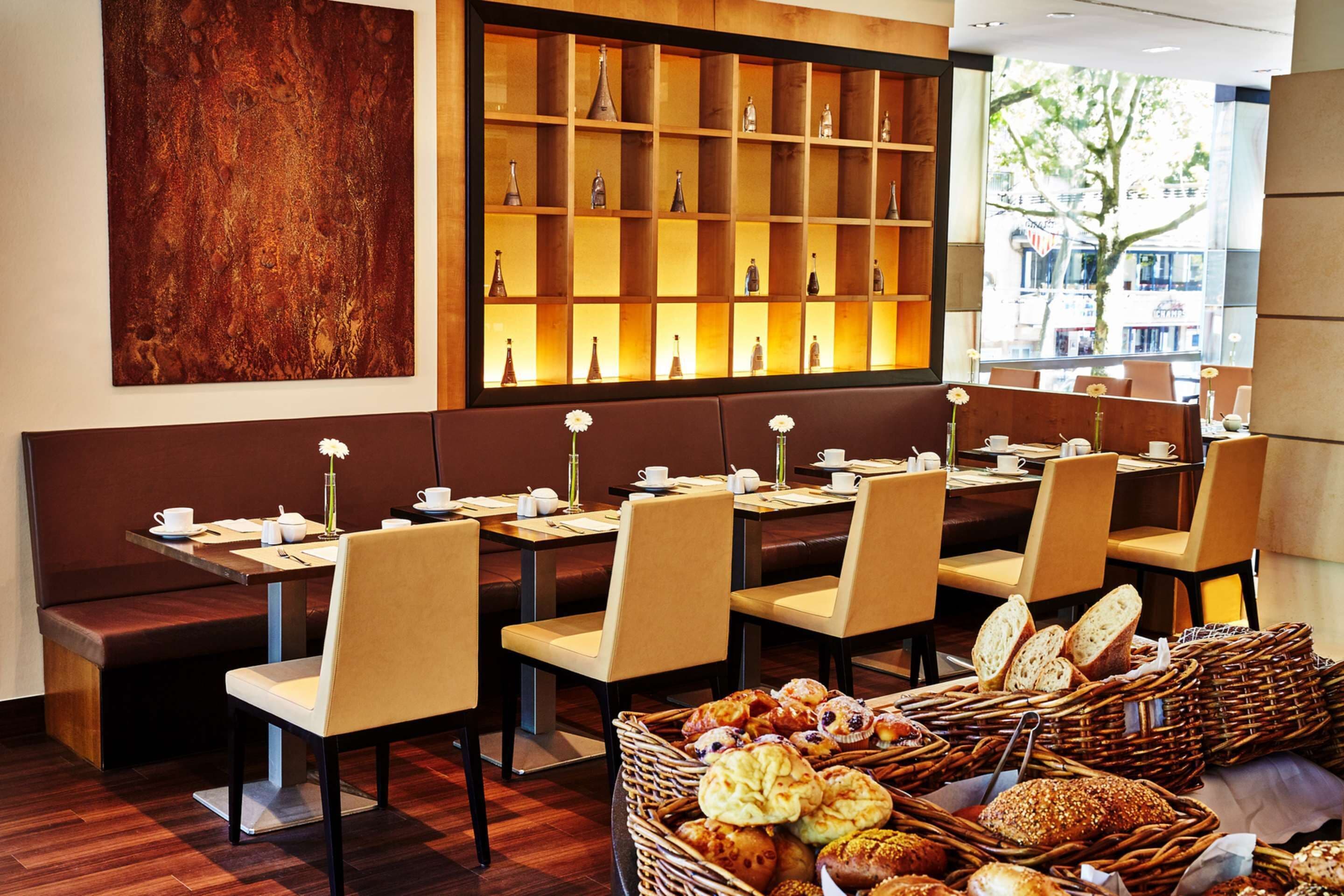 Un restaurant avec des banquettes et des tables, un mur décoré de vases et une variété de pains et de pâtisseries disposés sur les tables.