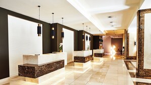 A hotel reception area with marble counters, pendant lighting, and a reflective tiled floor. - Steigenberger Hotel Köln (Cologne)