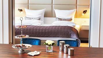 Habitación de hotel con cama, mesitas de noche, una mesa de comedor con sillas y una lámpara colgante decorativa.