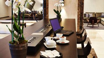 Vestíbulo de hotel con mostrador de recepción, una computadora portátil, estación de café y plantas de orquídeas.