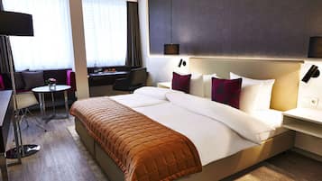 Quarto de hotel com uma cama grande, uma escrivaninha, uma cadeira e uma mesa pequena.