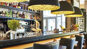 A bar area with multiple stools, a bar counter, and overhead lighting. - Steigenberger Hotel Köln (Cologne)