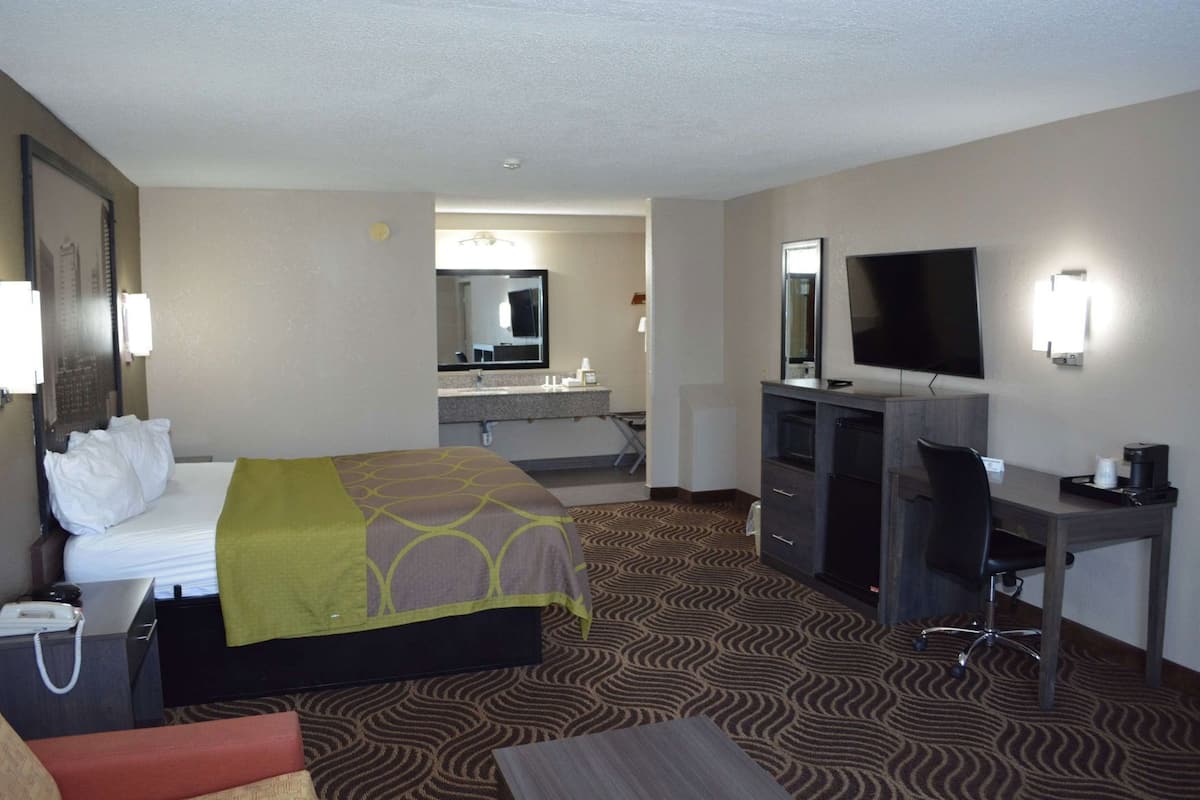 Une chambre d’hôtel avec un lit, un bureau, une chaise, une télévision et une salle de bain visible à travers une porte ouverte.