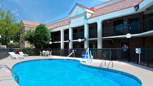 A swimming pool with a clear blue water, surrounded by a brick building with balconies and a covered walkway.