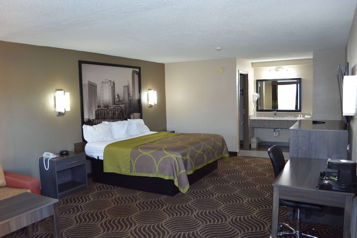 Une chambre d’hôtel comprenant un lit, un bureau, une chaise, une lampe de bureau, un téléphone, un miroir et une salle de bain avec un lavabo et des toilettes.