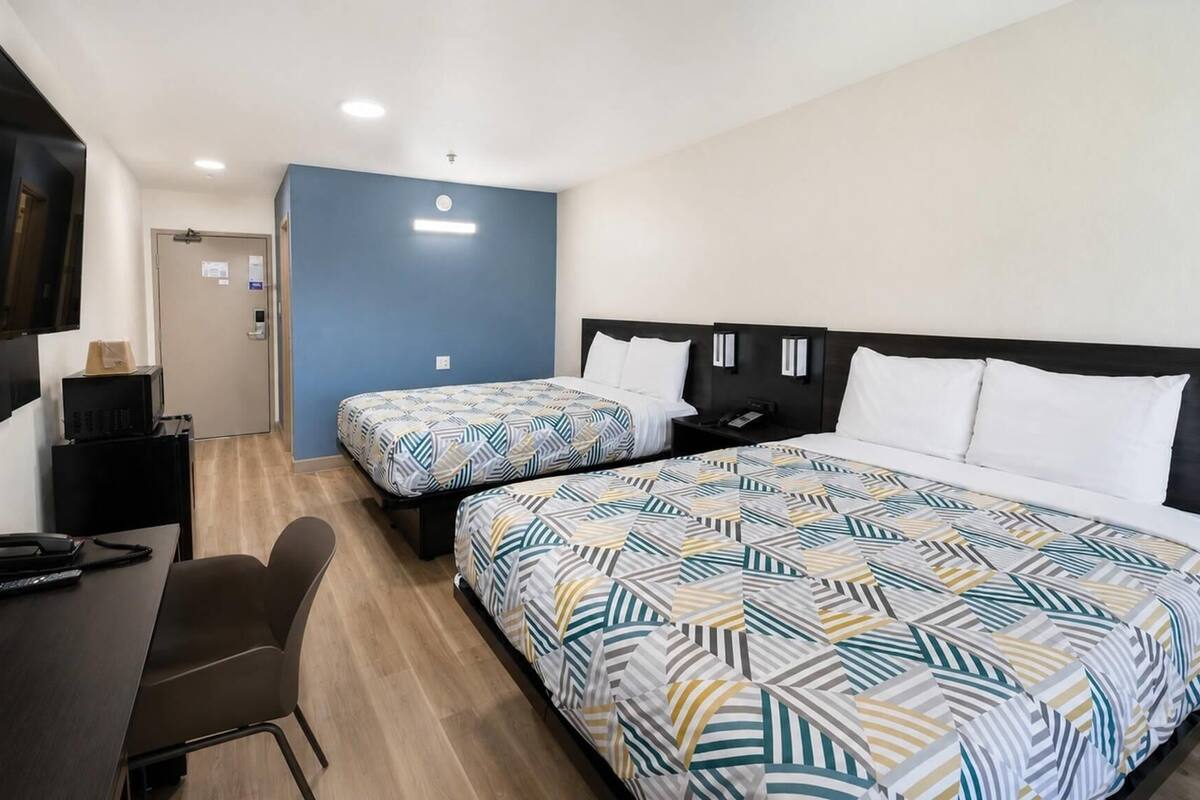 Een hotelkamer met twee bedden, een bureau met stoel, een televisie en een deur.