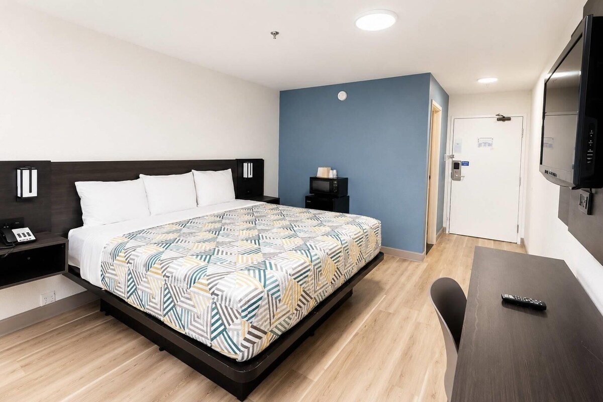 Habitación de hotel con cama, mesita de noche, televisor y escritorio con silla.