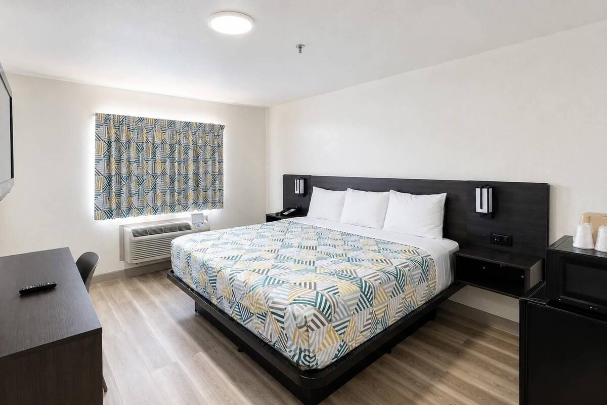 Een hotelkamer met een bed, nachtkastjes, een bureau, een televisie en een raam met gordijnen met een patroon.