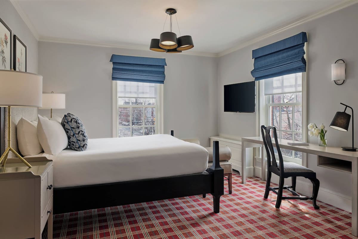 Ett hotellrum med en säng, ett skrivbord, en stol och en tv på väggen.