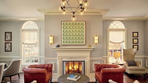 A room with a fireplace, two red leather sofas, a round coffee table, and a chandelier. - Morrison House Old Town Alexandria, Autograph Collection (Alexandria)