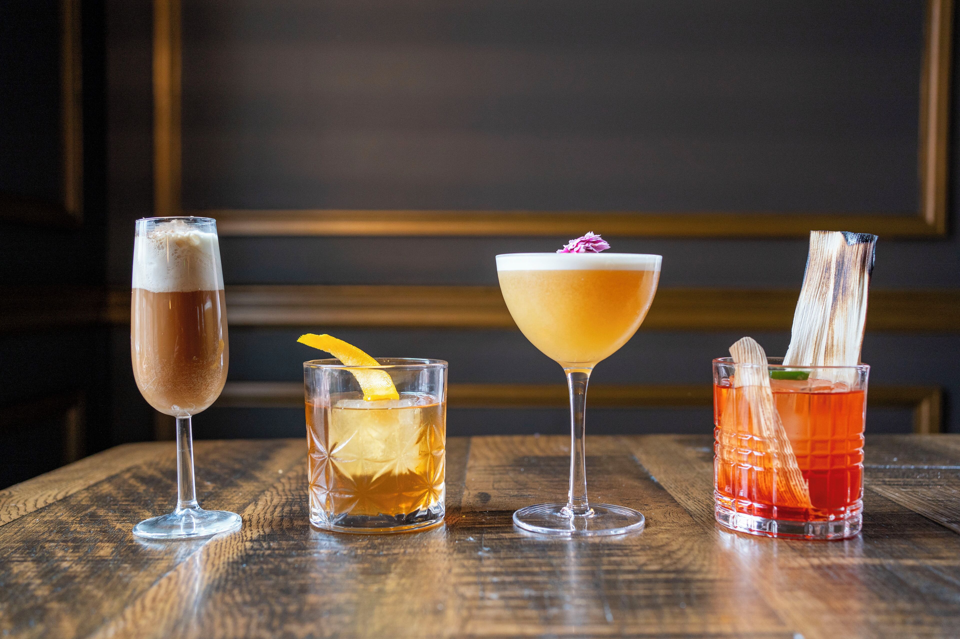 Vier verschiedene Cocktails auf einem Holztisch.