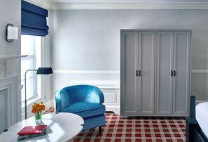 A room with a blue sofa, a white table with a vase of flowers, a large wardrobe, and a red patterned carpet.