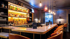 A bar area with a marble countertop, leather bar stools, and shelves stocked with bottles and glasses. - Morrison House Old Town Alexandria, Autograph Collection (Alexandria)