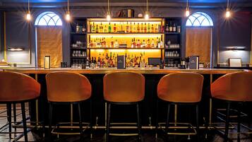 Uma área de bar com um balcão comprido, várias prateleiras cheias de garrafas e três banquetas laranjas.