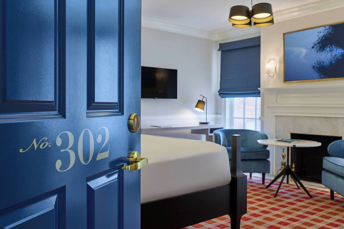 Ett hotellrum med en stor säng, ett skrivbord, en stol, en tv och en öppen spis.