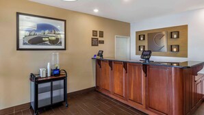 A reception area with a wooden counter, a digital payment terminal, a framed cityscape picture, a cart with bottled water, and a wall-mounted clock.