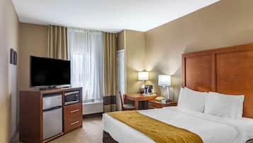 A hotel room with a bed, a desk, a television, a refrigerator, and a lamp.