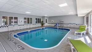 A swimming pool with a tiled floor, poolside chairs, and a ceiling with recessed lighting.