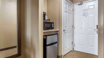 Un pasillo con microondas, refrigerador y una puerta con letrero de salida de emergencia.